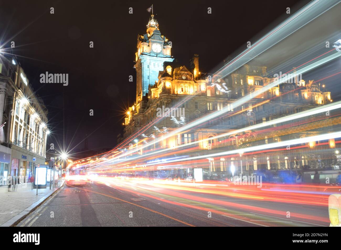 Guardando lungo Princes Street Edinburgh con sentieri leggeri dal passaggio di veicoli verso l'hotel Scotsman. Foto Stock