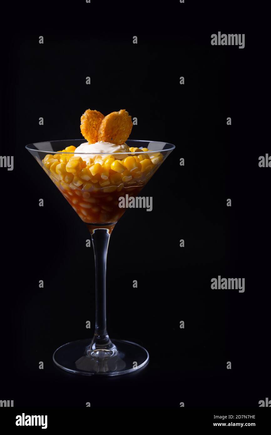 Insalata di fagioli, mais e crostini in un bicchiere di martini. Sfondo nero, tasto basso, primo piano. Concetto. Foto Stock