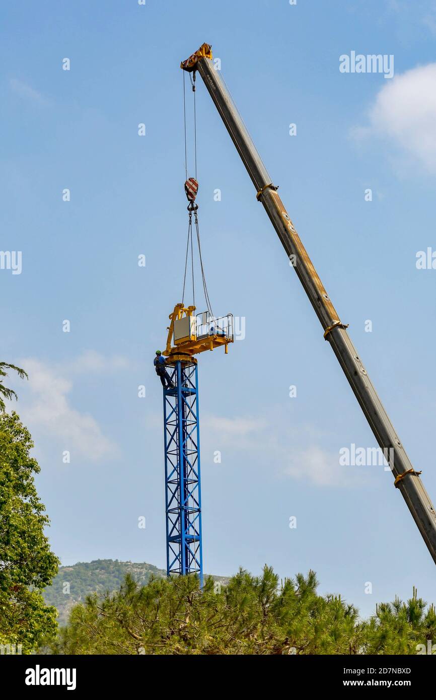 LENNO, LAGO DI COMO, ITALIA - GIUGNO 2019: Operatore specializzato con imbracatura sopra una gru a torre in fase di smontaggio con l'aiuto di una gru telescopica Foto Stock