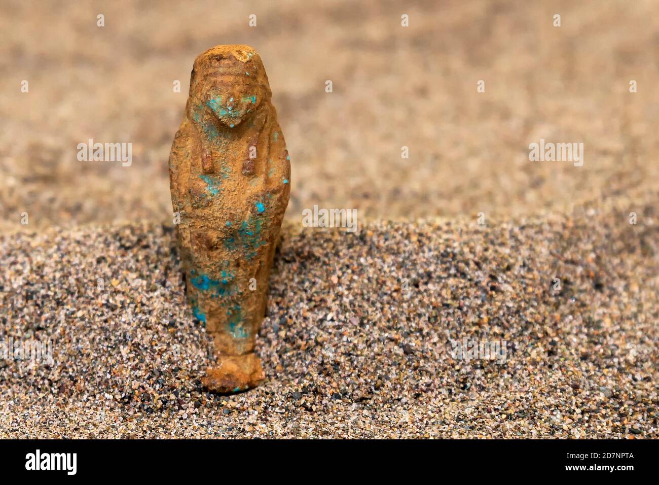 Uno sshabti egiziano antico, molto indossato, in piedi nella sabbia. Profondità di campo poco profonda. Foto Stock