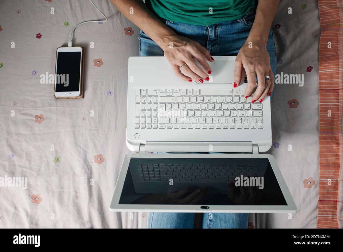 Dall'alto del raccolto anonimo freelance femminile seduto a letto vicino allo smartphone e digitando le informazioni sulla tastiera del computer portatile durante il lavoro a distanza da ho Foto Stock