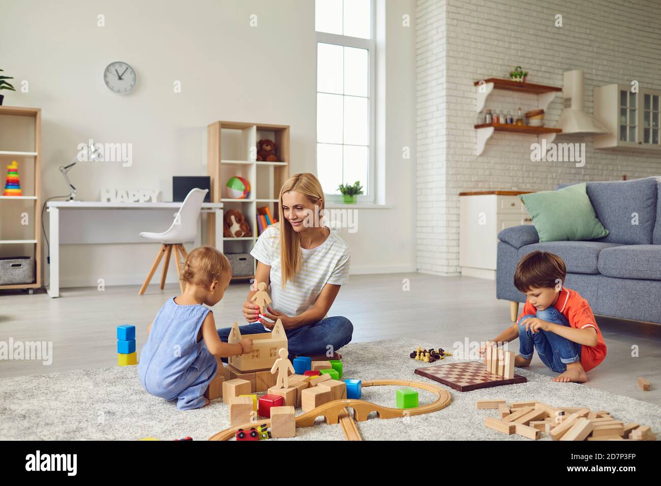 Madre felice e i suoi due bambini a casa, giocando con un sacco di blocchi di legno, la costruzione di una grande città giocattolo Foto Stock