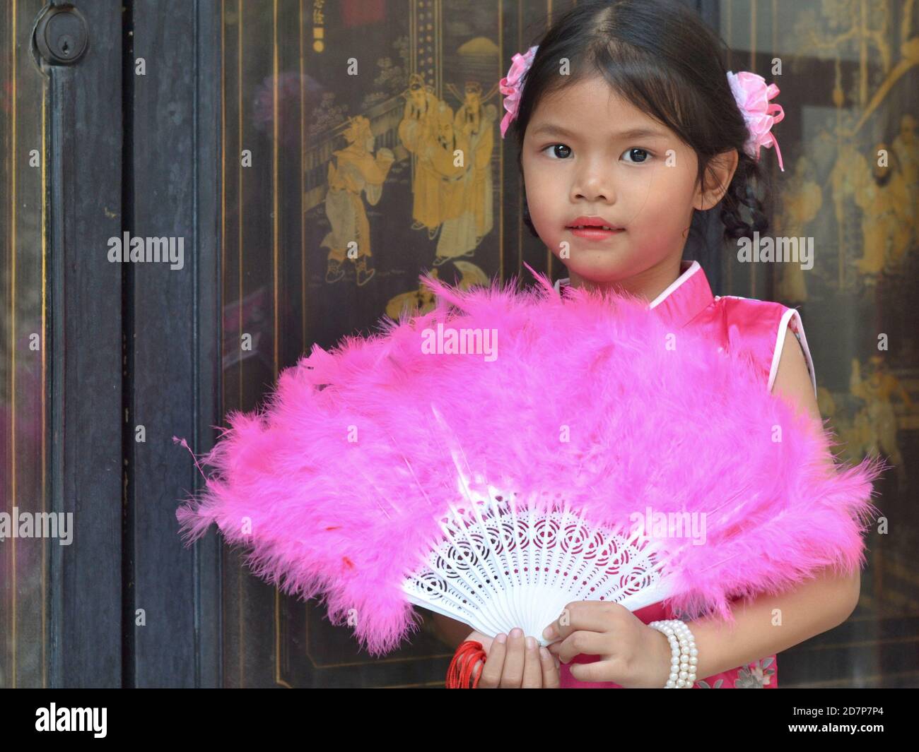 Vestita carina ragazza cinese tailandese pose con un fan di piume rosa tenuto a mano, durante il Capodanno cinese, all'interno del Tempio del Drago Lotus. Foto Stock