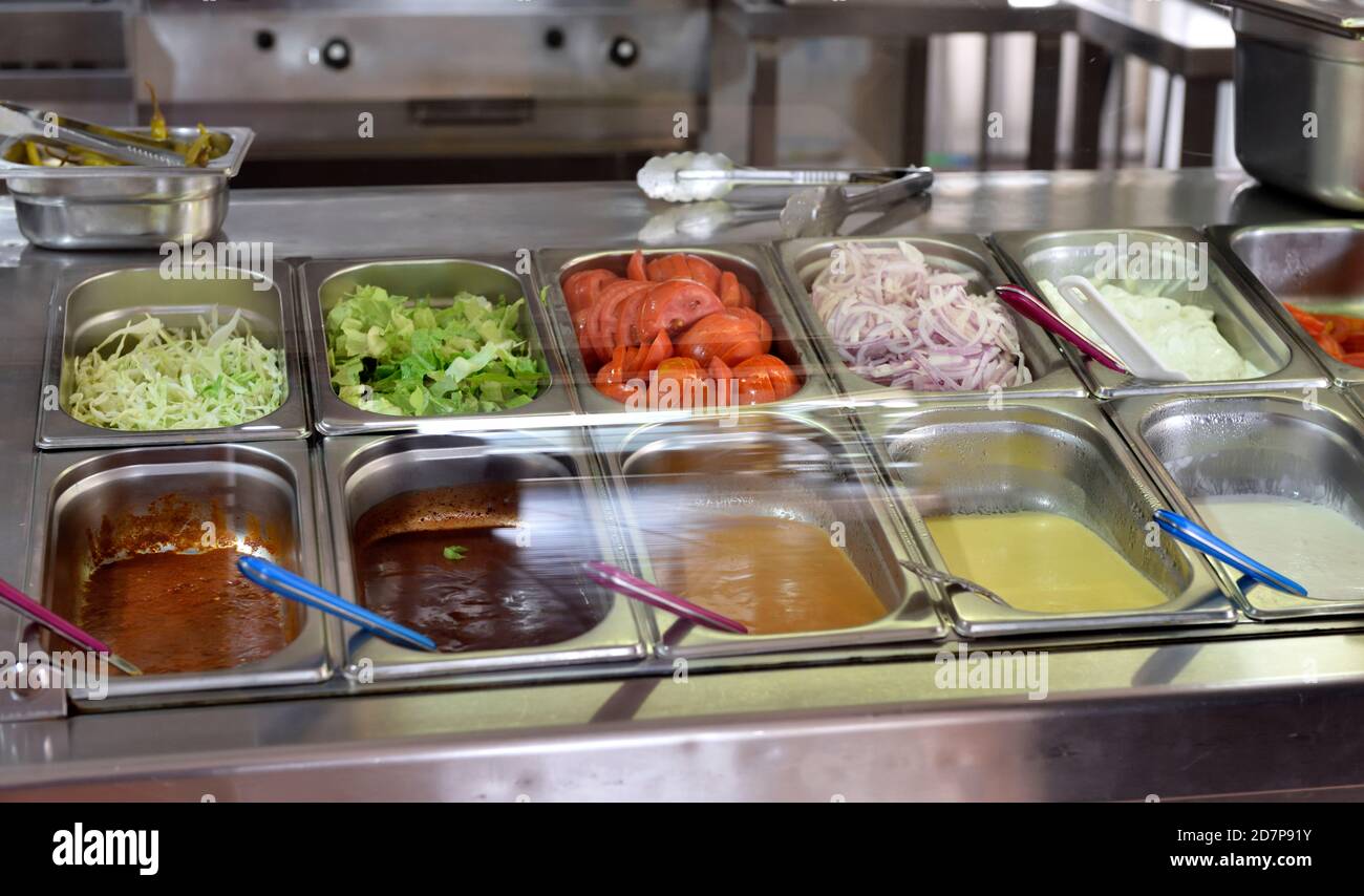 Ingredienti per insalate e condimenti in tegole di acciaio inossidabile dietro lo schermo trasparente per l'uso in giros, kebab, hamburger, ecc. nel ristorante Foto Stock