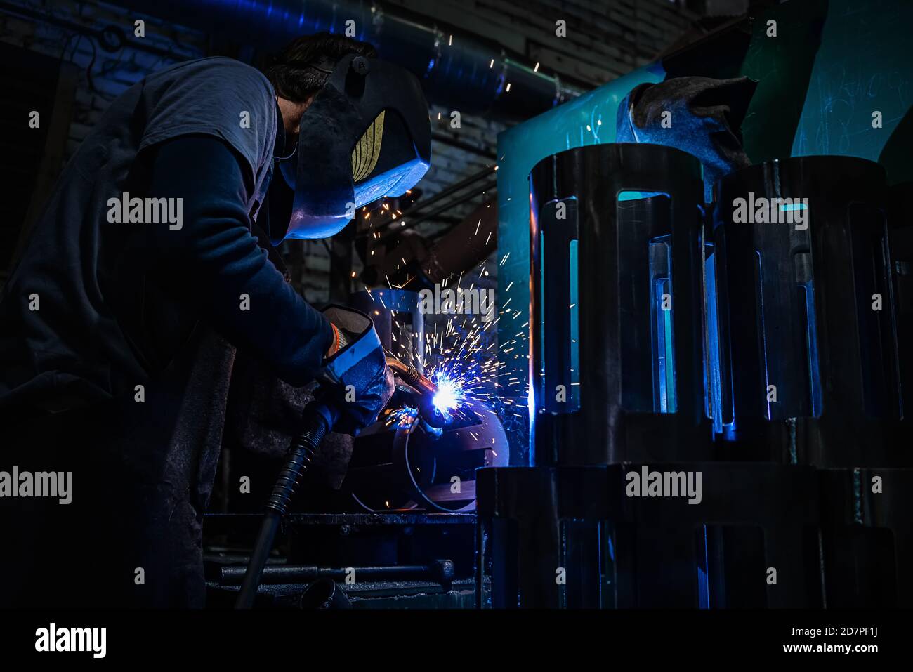 Vista laterale del saldatore nel casco protettivo dettaglio di metallo per saldatura con scintille in fabbrica Foto Stock