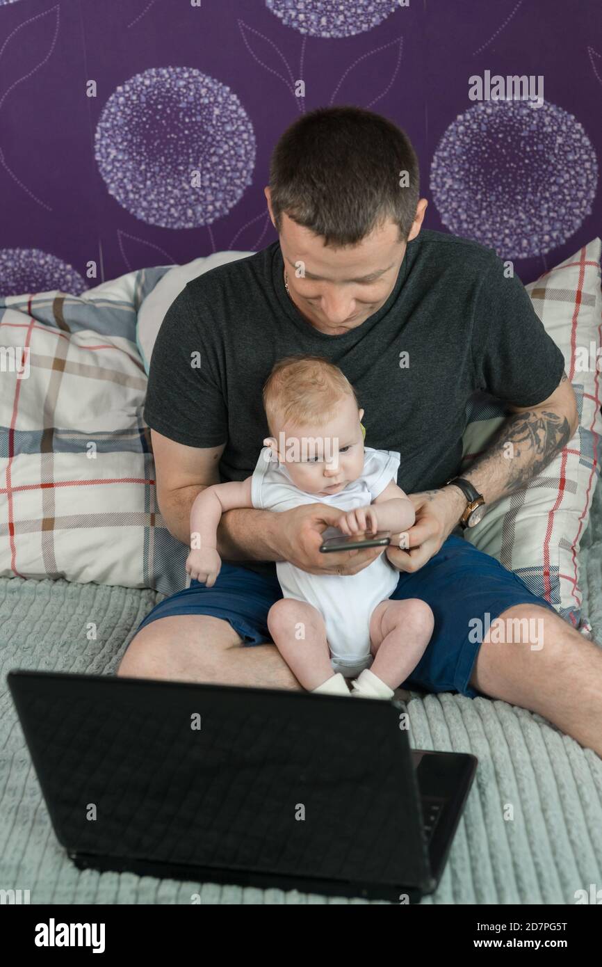 Un uomo con un bambino piccolo che guarda uno smartphone a casa. Lavoro a casa. La comunicazione remota Foto Stock