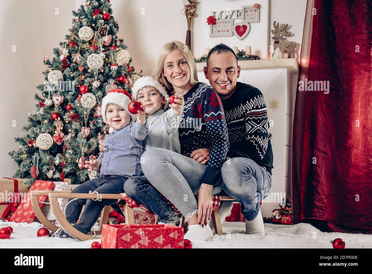 Due bambini piccoli con madre e padre seduti sulla slitta E festeggia il Natale - buona famiglia Foto Stock