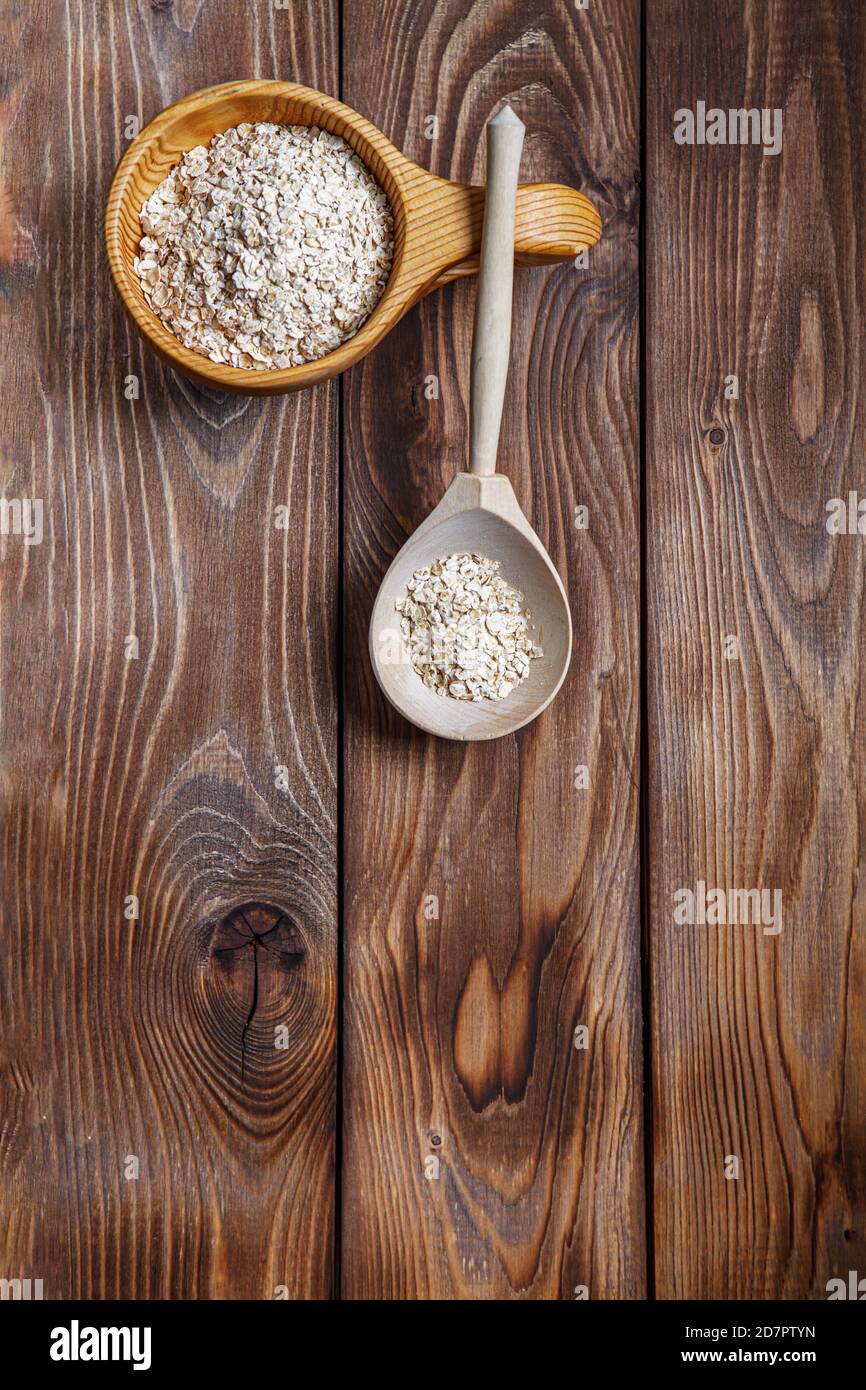 Tazza di legno e cucchiaio con farinata d'avena. Il concetto di alimentazione sana. Struttura in legno. Layout piatto. Spazio di copia Foto Stock