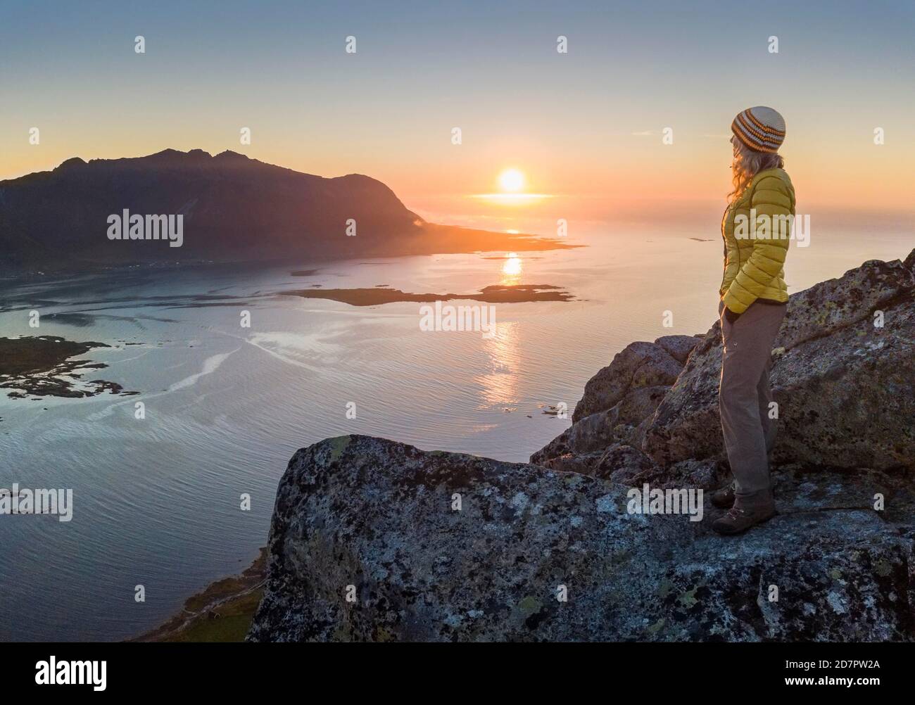 Donna in piedi sulla cima di Hoven al tramonto, dietro mare e fiordo, Vagan, Lofoten, Nordland, Norvegia Foto Stock