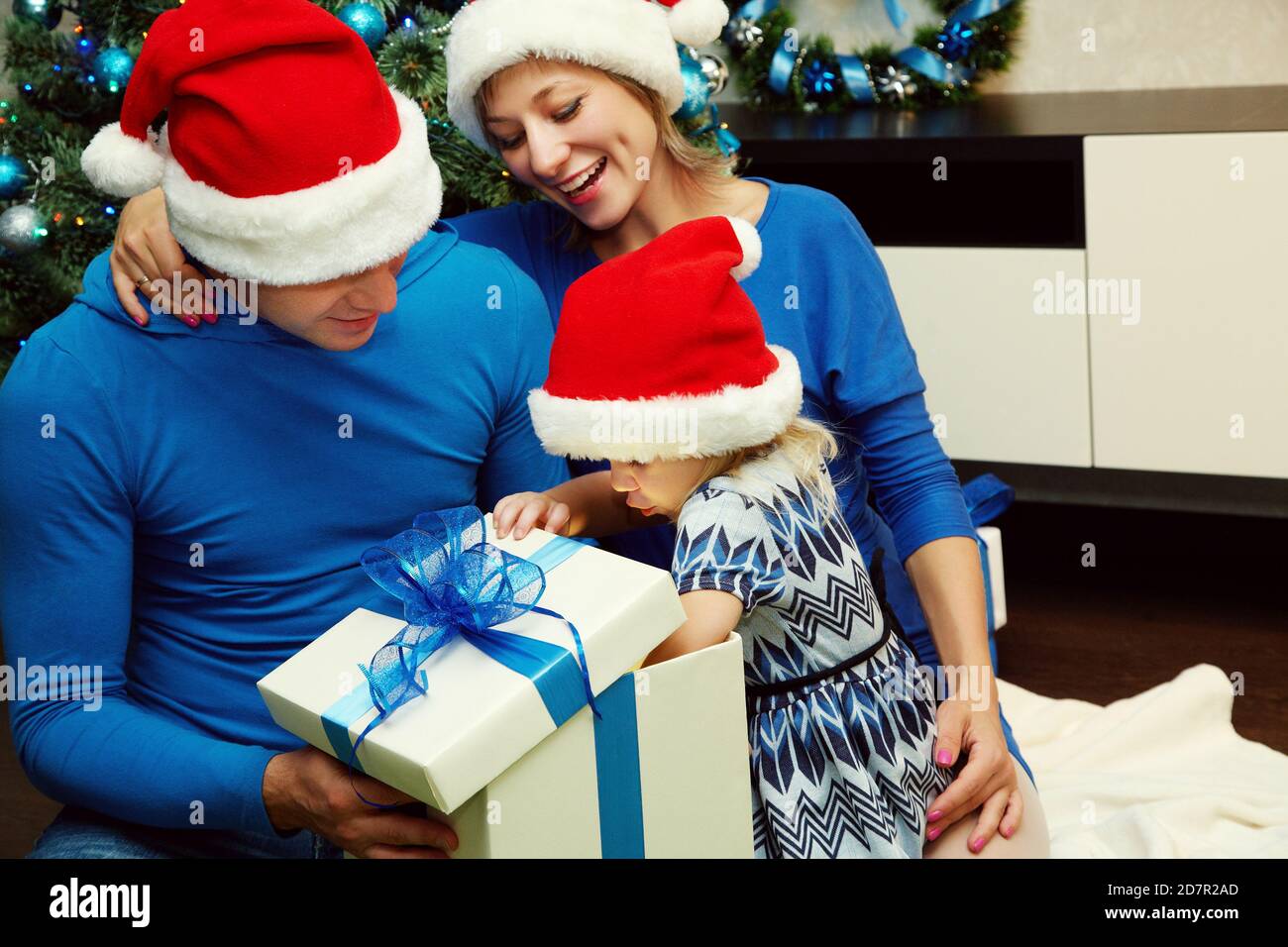 La giovane famiglia festeggia il Natale a casa, padre e madre danno un regalo al bambino Foto Stock