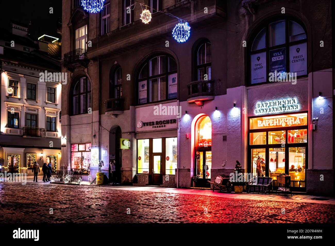 Lviv, Ucraina - 27 dicembre 2019: Piazza del mercato della città vecchia con la gente di notte da caffè, negozi e negozi di Yves Rocher Francia e Varenik ristorante Foto Stock