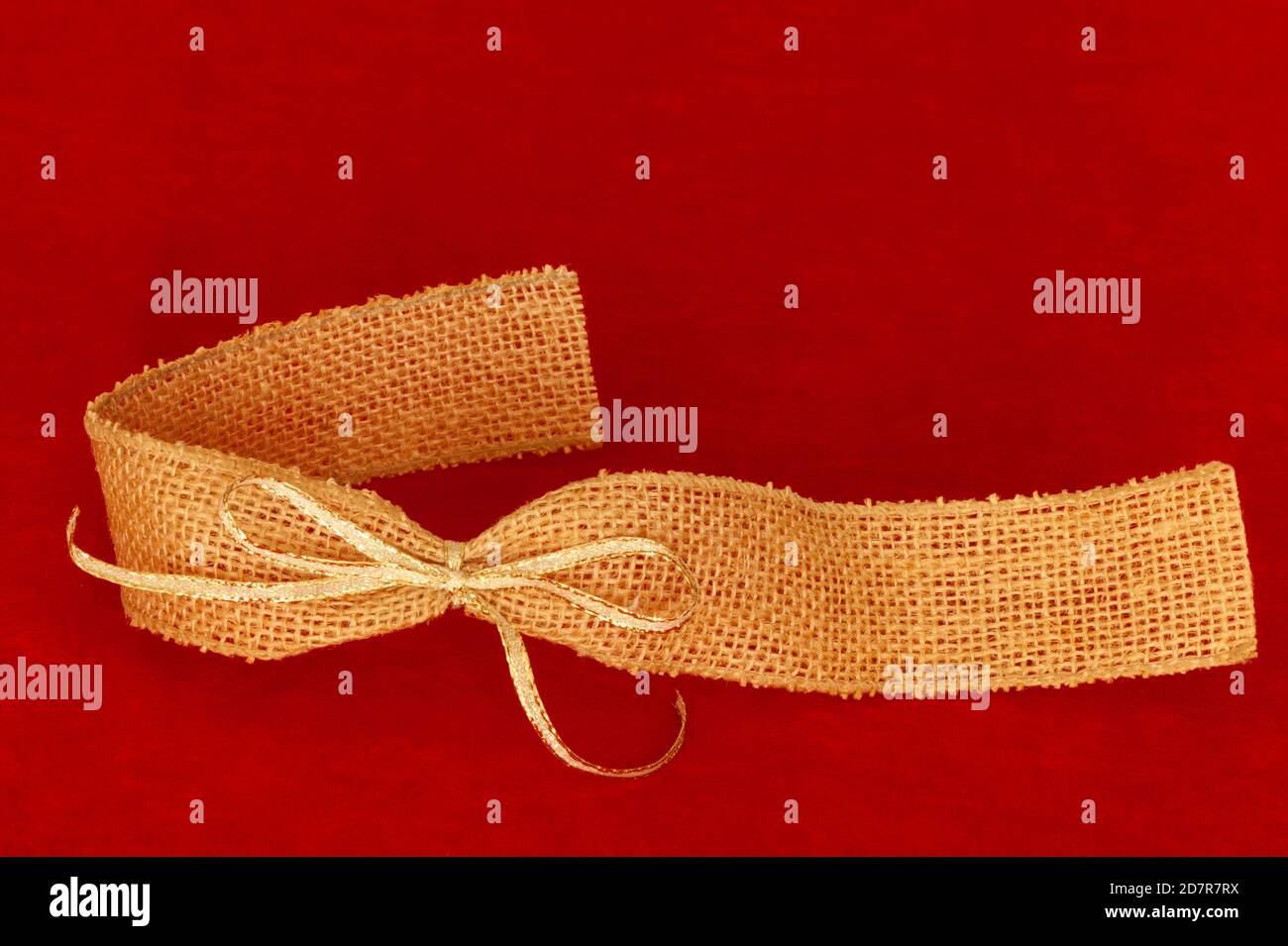 Primo piano del nastro su sfondo rosso. Spazio di testo nella parte superiore con borlap e nastro legato in oro nella parte inferiore. Foto Stock