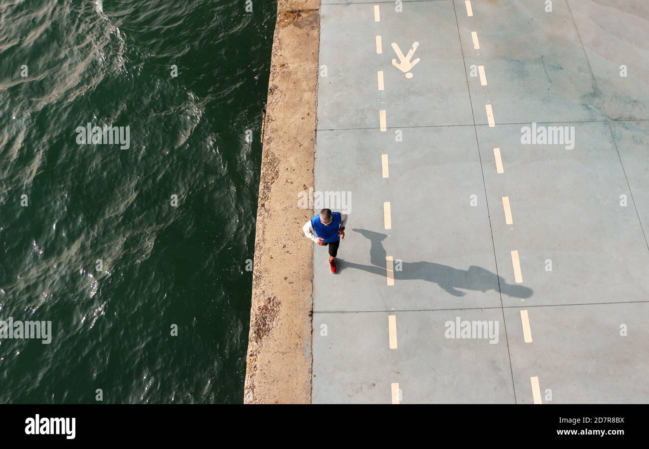 Lone Jogger maschio visto dall'alto che corre lungo la baia Di Santander Cantabria Spagna sotto il centro artistico del Botin Centre In una soleggiata mattina di ottobre Foto Stock