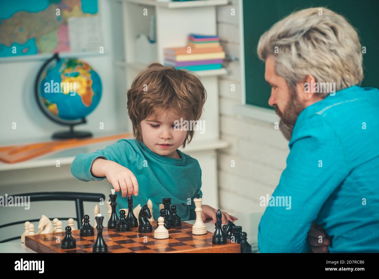 Ragazzo concentrato che sviluppa la strategia degli scacchi. Ragazzo carino che sviluppa la strategia degli scacchi. Bel maestro che dà lezioni private di scacchi al ragazzo prescolare. Foto Stock