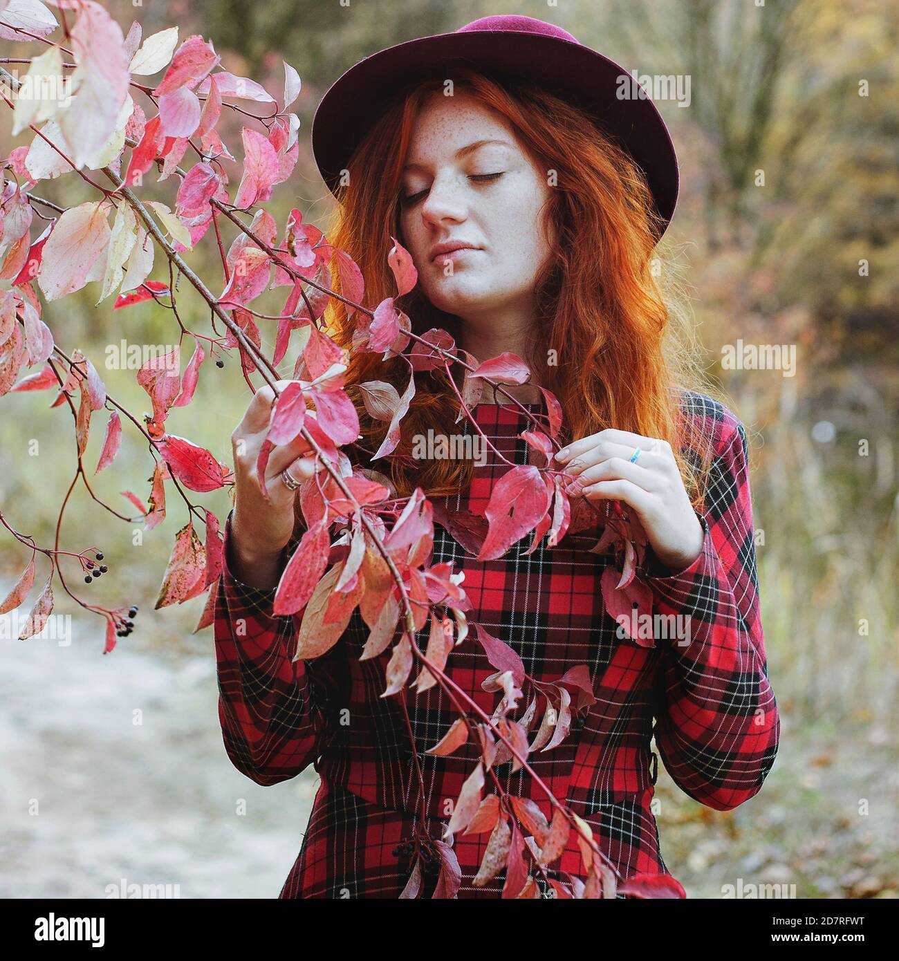 ragazza con capelli rossi e fracelle in abito rosso e. cappello sognando nella colorata foresta d'autunno Foto Stock