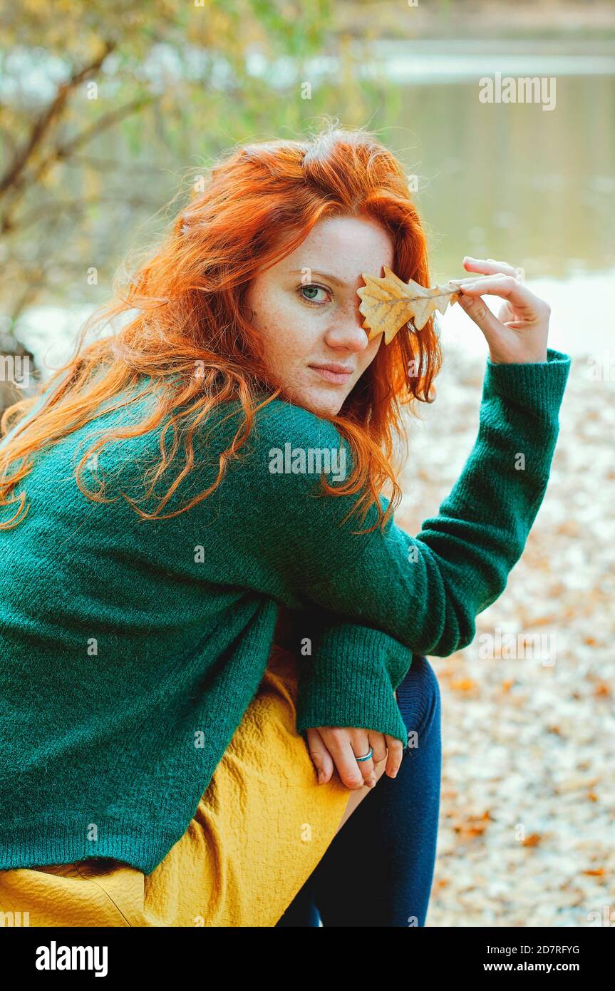 Divertente ritratto di giovane donna rossa con foglia gialla d'autunno nelle mani nel parco. Foto Stock