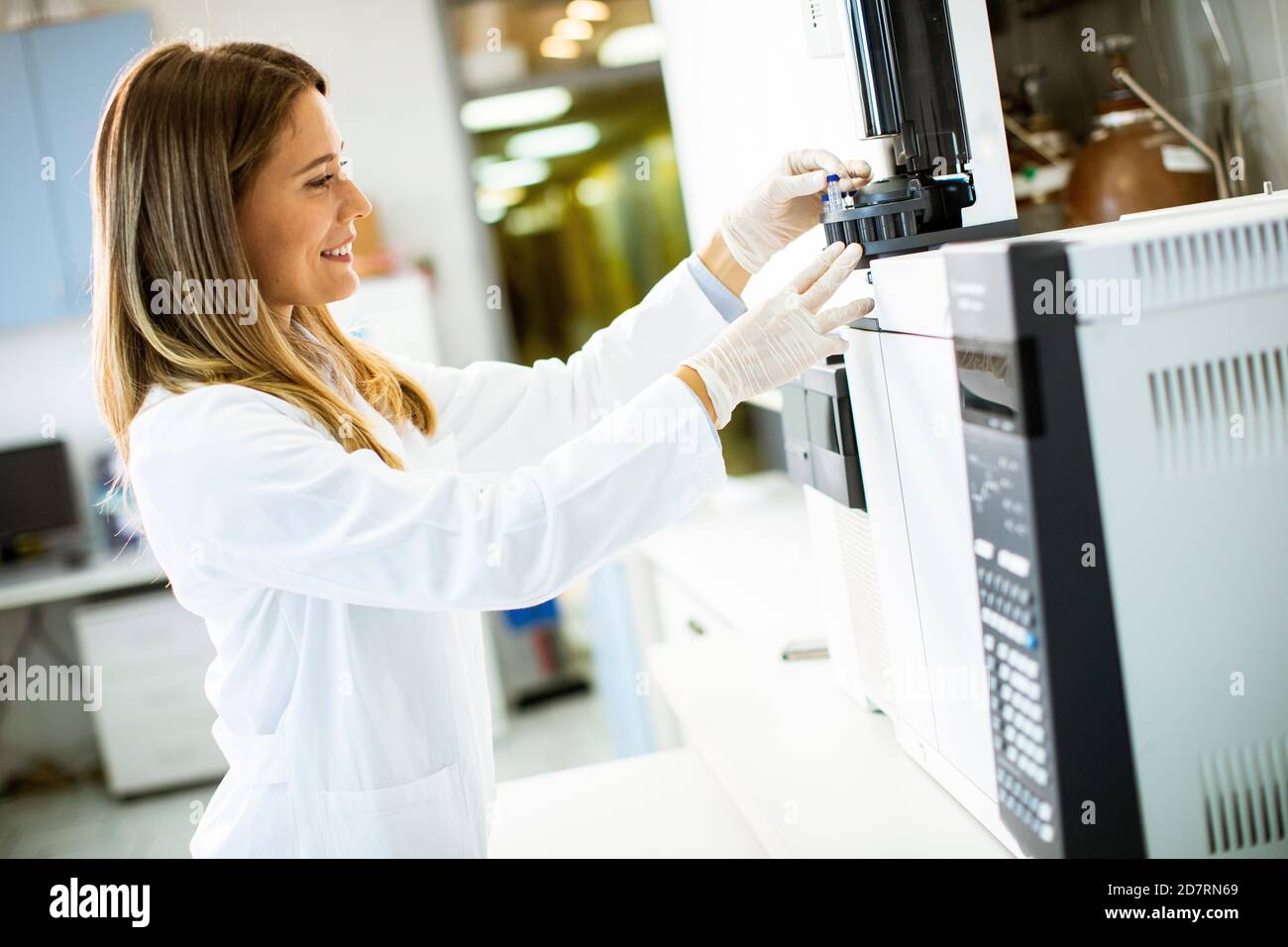 Giovane scienziata femminile in un flaconcino bianco di messa camice da laboratorio con un campione per un'analisi su gascromatografo in laboratorio biomedico Foto Stock