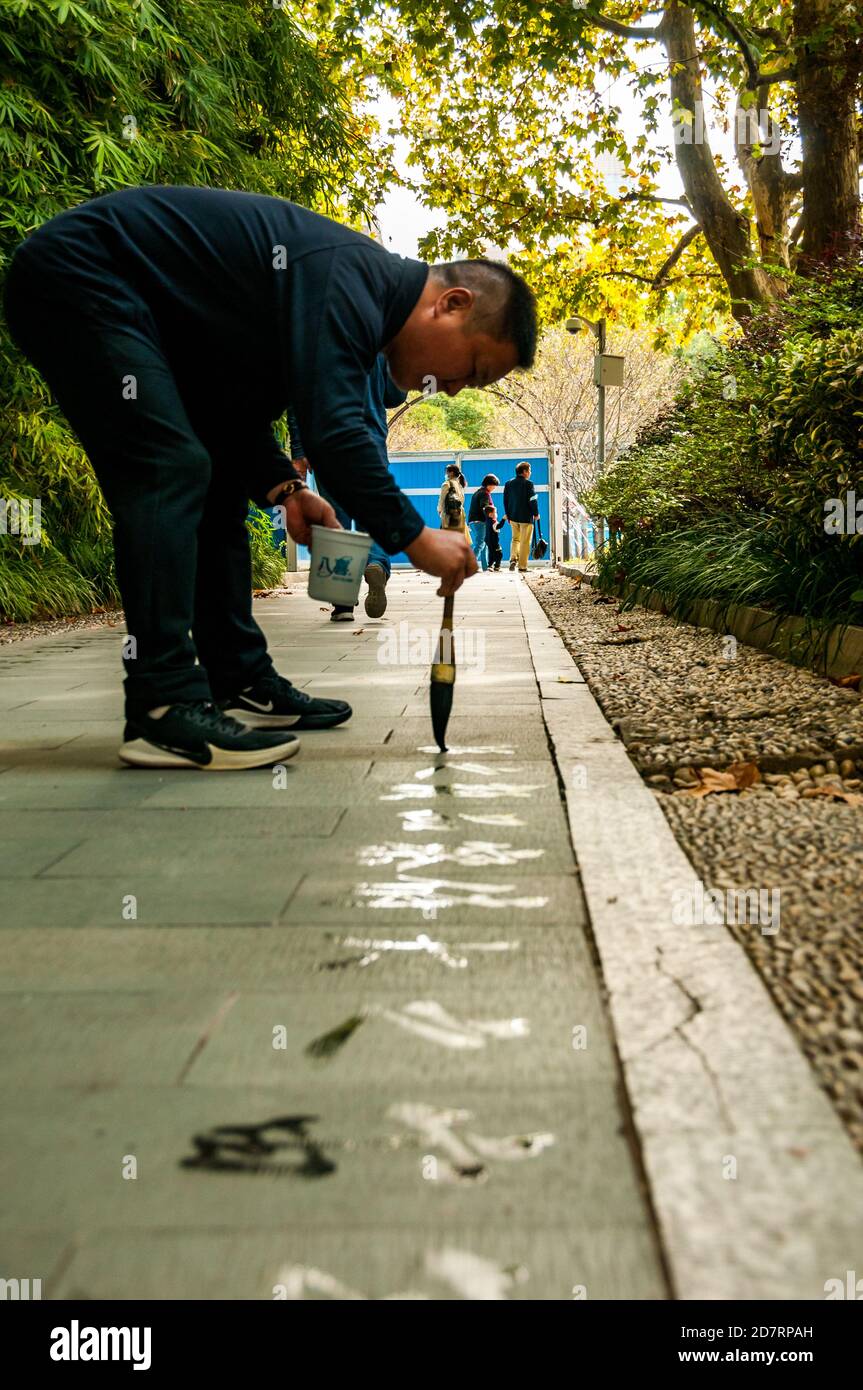 Un uomo scrive la calligrafia usando un pennello ad acqua nella Piazza del Popolo di Shanghai. Foto Stock