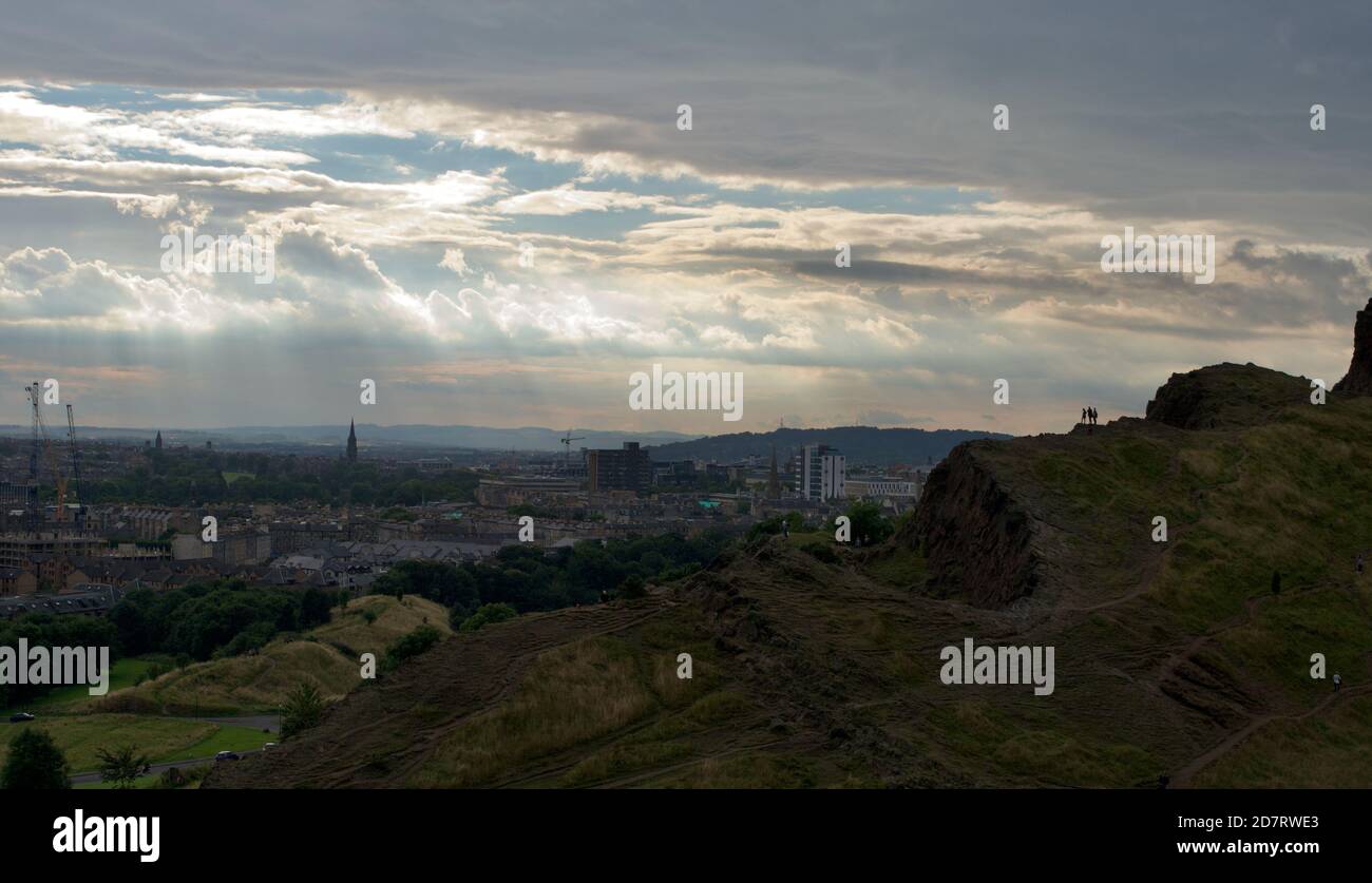 La vista da Arthur's Seat, Edimburgo, Scozia (Regno Unito): Skyline degli edifici della città, luce dorata che oscura le nuvole; sagome delle persone Foto Stock