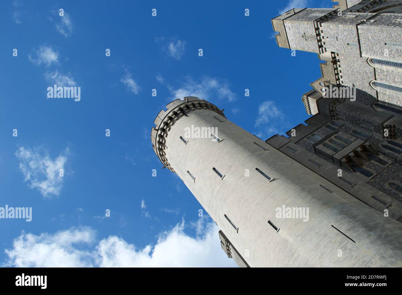 Guardando in alto le merlature illuminate di una torre rotonda su un antico castello tradizionale in pietra (Inglese / britannico / europeo) contro il cielo blu in (Aru Foto Stock