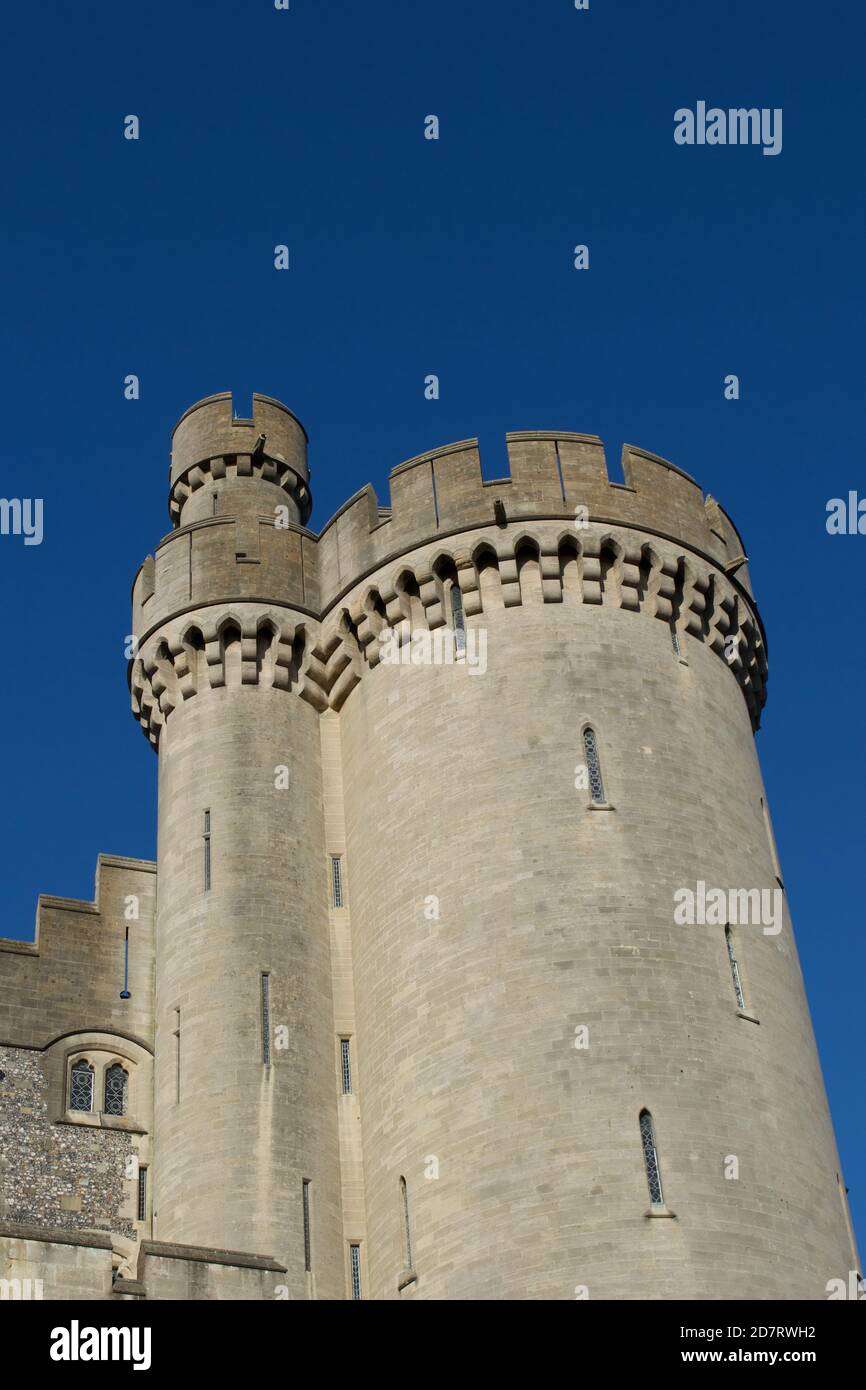 Guardando in alto le merlature illuminate di una torre rotonda su un antico castello tradizionale in pietra (Inglese / britannico / europeo) contro il cielo blu in (Aru Foto Stock
