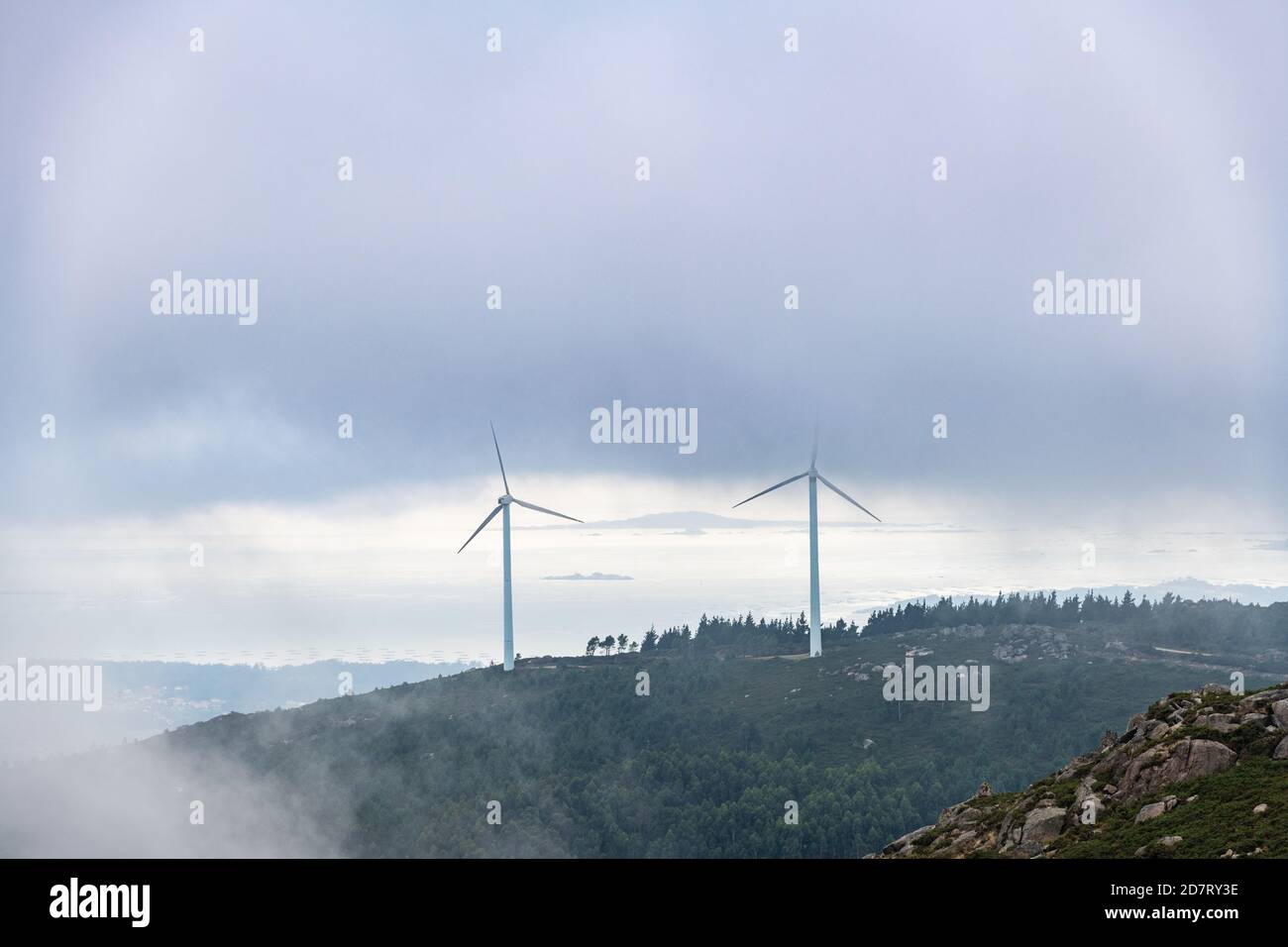 Vista aerea dell'estuario della Ria de Arousa dal monte Muralla in un pomeriggio estivo foggoso, con alcune turbine eoliche tra le nuvole. Foto Stock