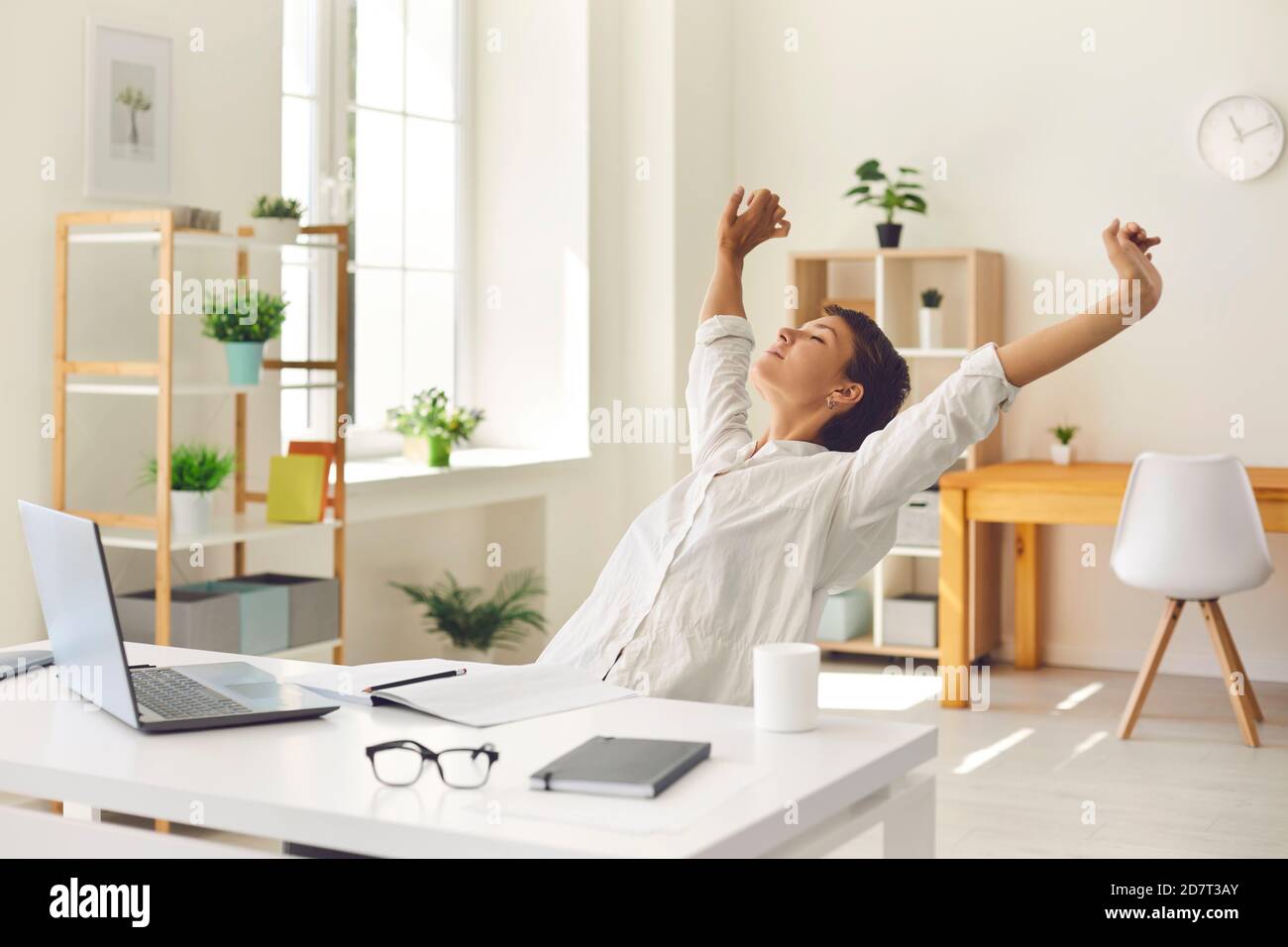 Donna d'affari seduta alla scrivania dell'ufficio, prendente la rottura dal lavoro e stretching i muscoli rigidi e tesi Foto Stock