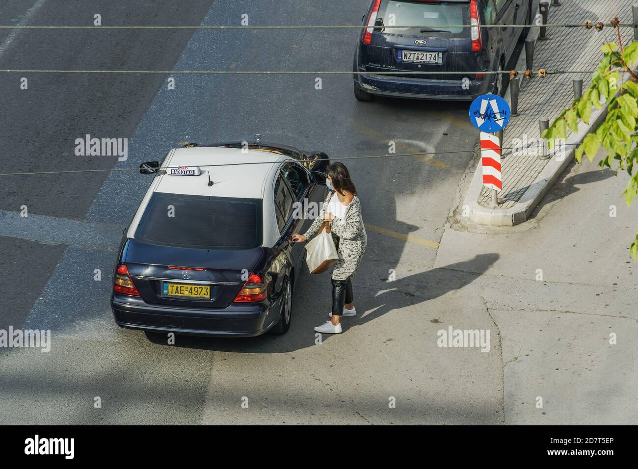 Donna con maschera covid-19 pronta ad entrare in taxi. Una donna non identificata con protezione facciale che entra in un taxi blu e bianco su una strada pubblica a Salonicco, Grecia. Foto Stock