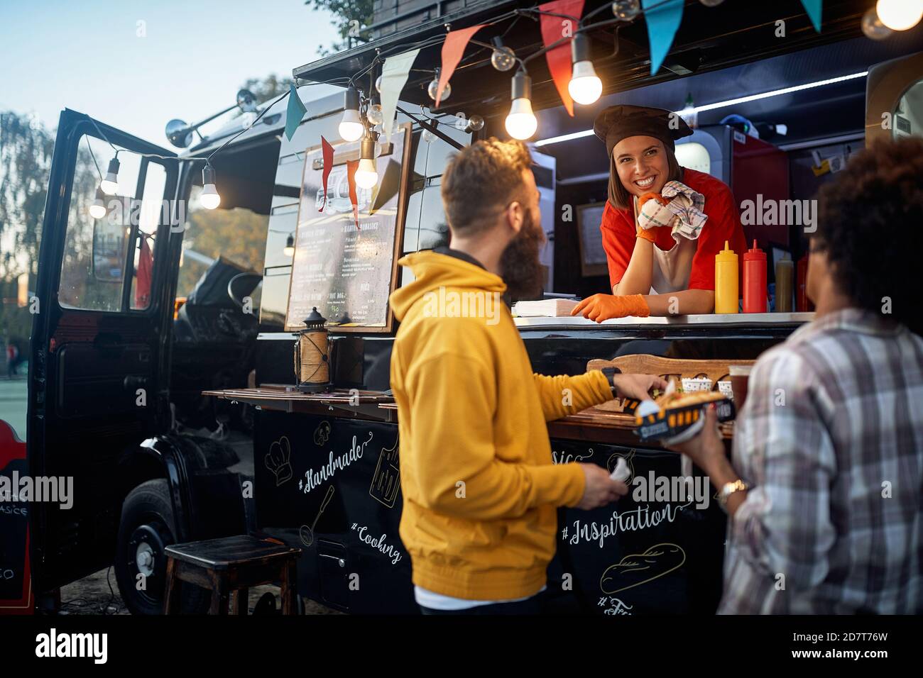 amici che hanno buon tempo a mangiare di fronte al fast food, parlando con la dipendente caucasica femminile Foto Stock