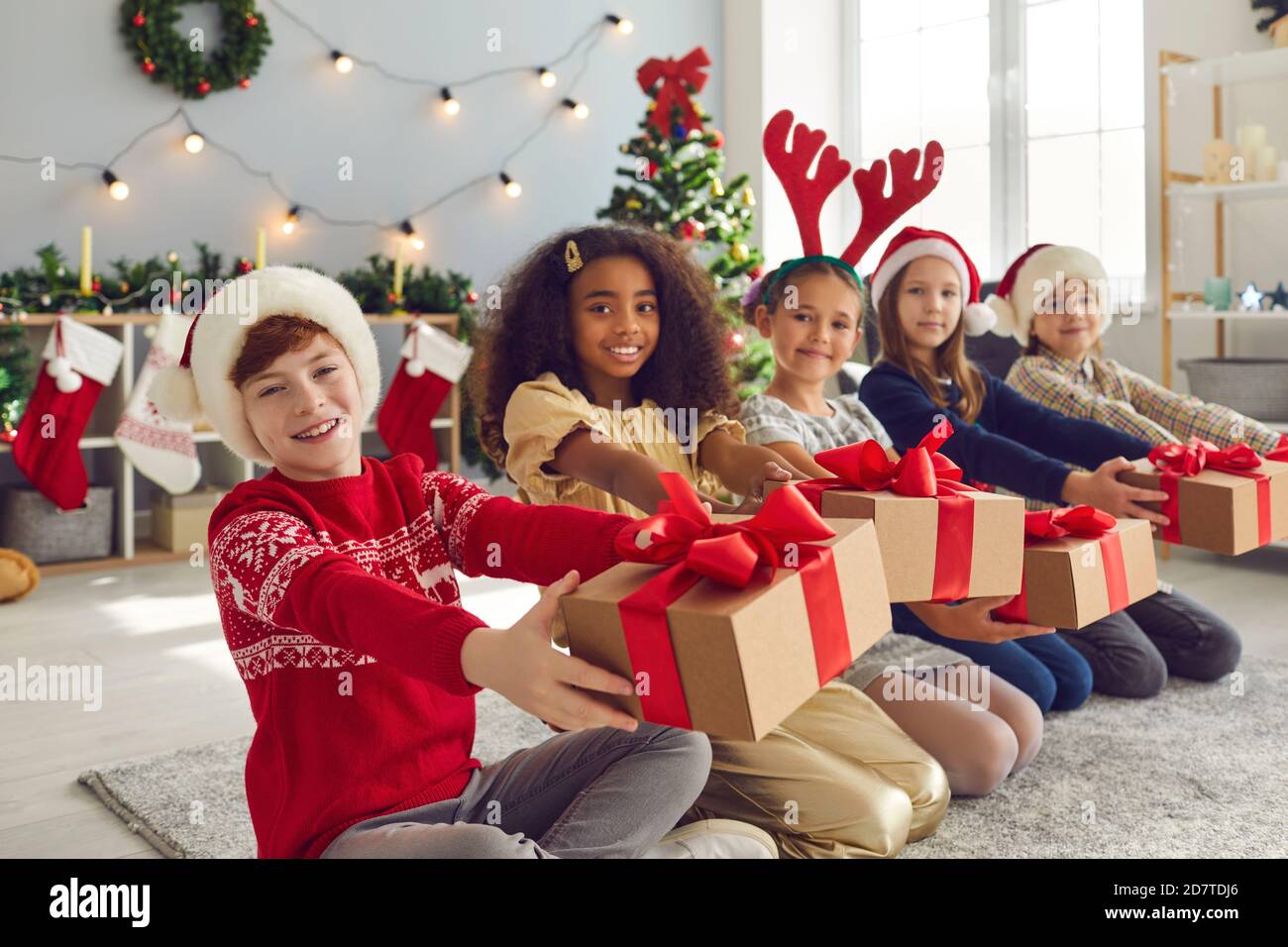 Gruppo di felici bambini sorridenti seduti di fila in soggiorno E regali di Natale Foto Stock