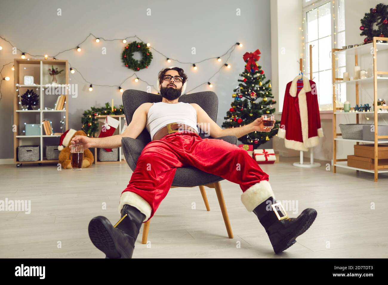 Il giovane beve alcolici e si rilassa in poltrona dopo la festa Difficile la notte di Natale Foto Stock