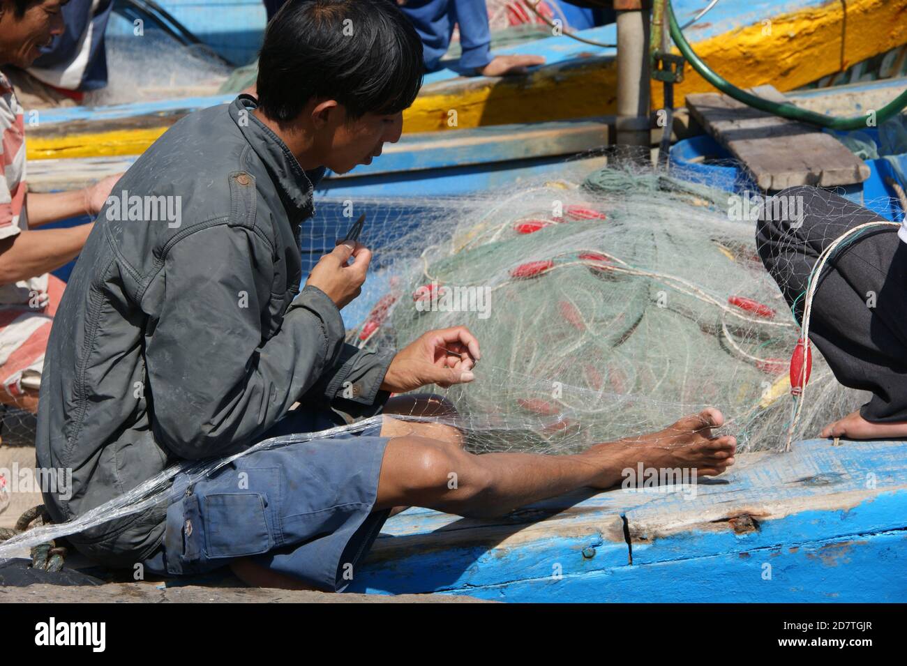 Il giovane pescatore usò le mani e i piedi quando si menda le reti. Foto Stock
