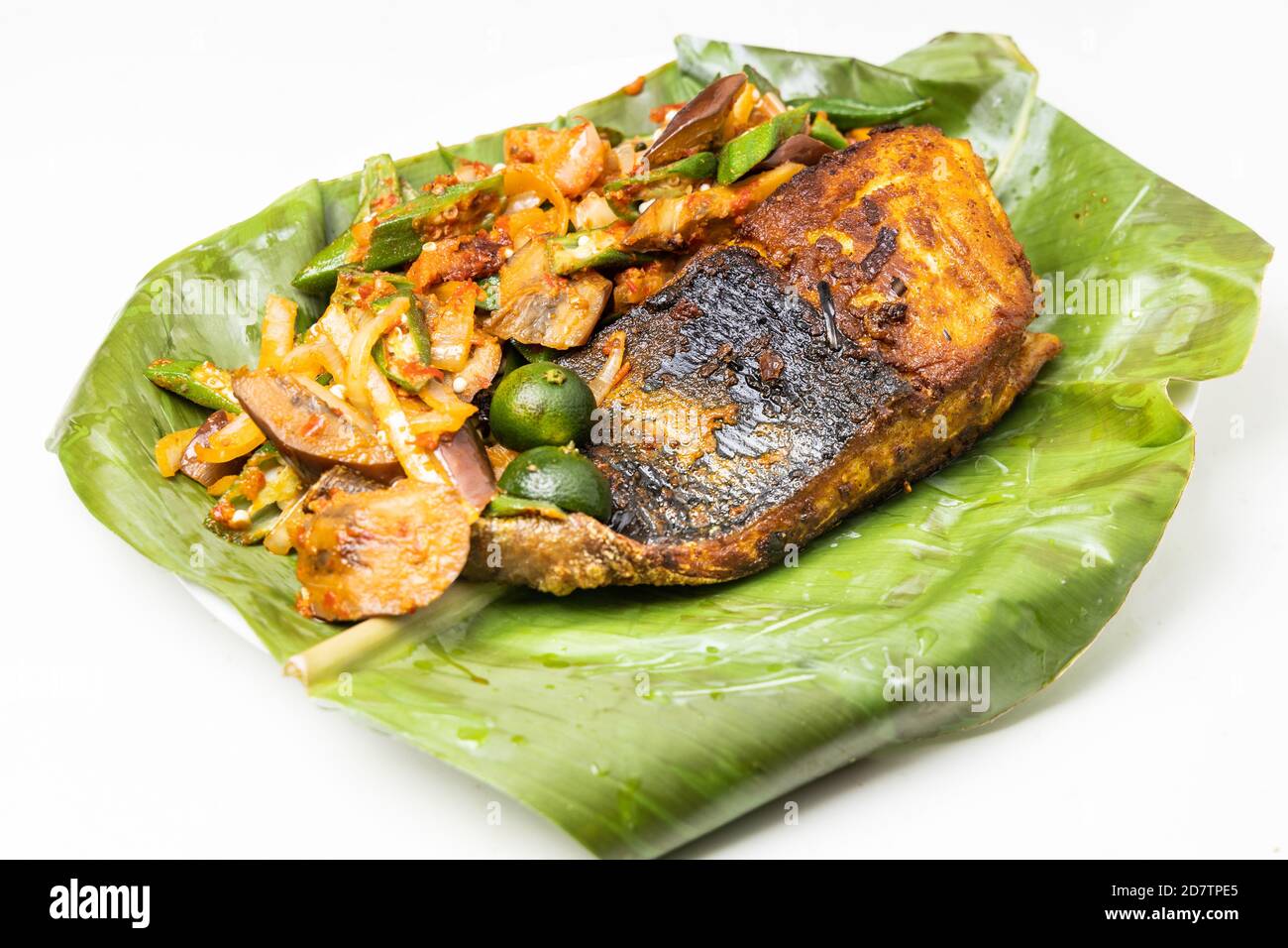 Popolare pesce di stingray alla griglia con spezie e verdure servite sopra foglia di banana Foto Stock