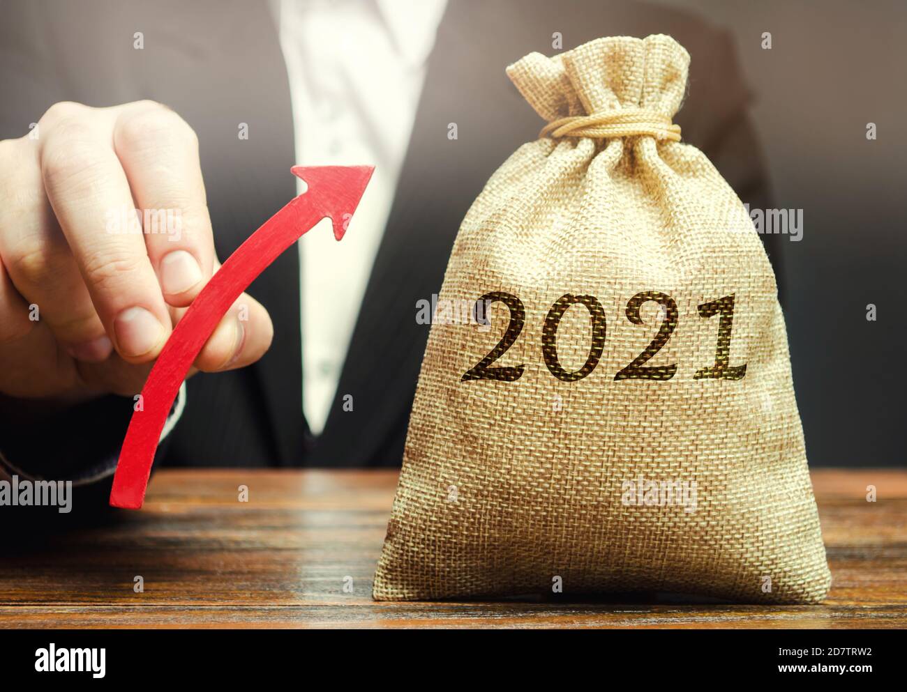 Uomo d'affari tiene una freccia in su vicino alla borsa di soldi 2021. Pianificazione strategica e di bilancio. Visione. Previsioni aziendali. Crescita e sviluppo del business Foto Stock