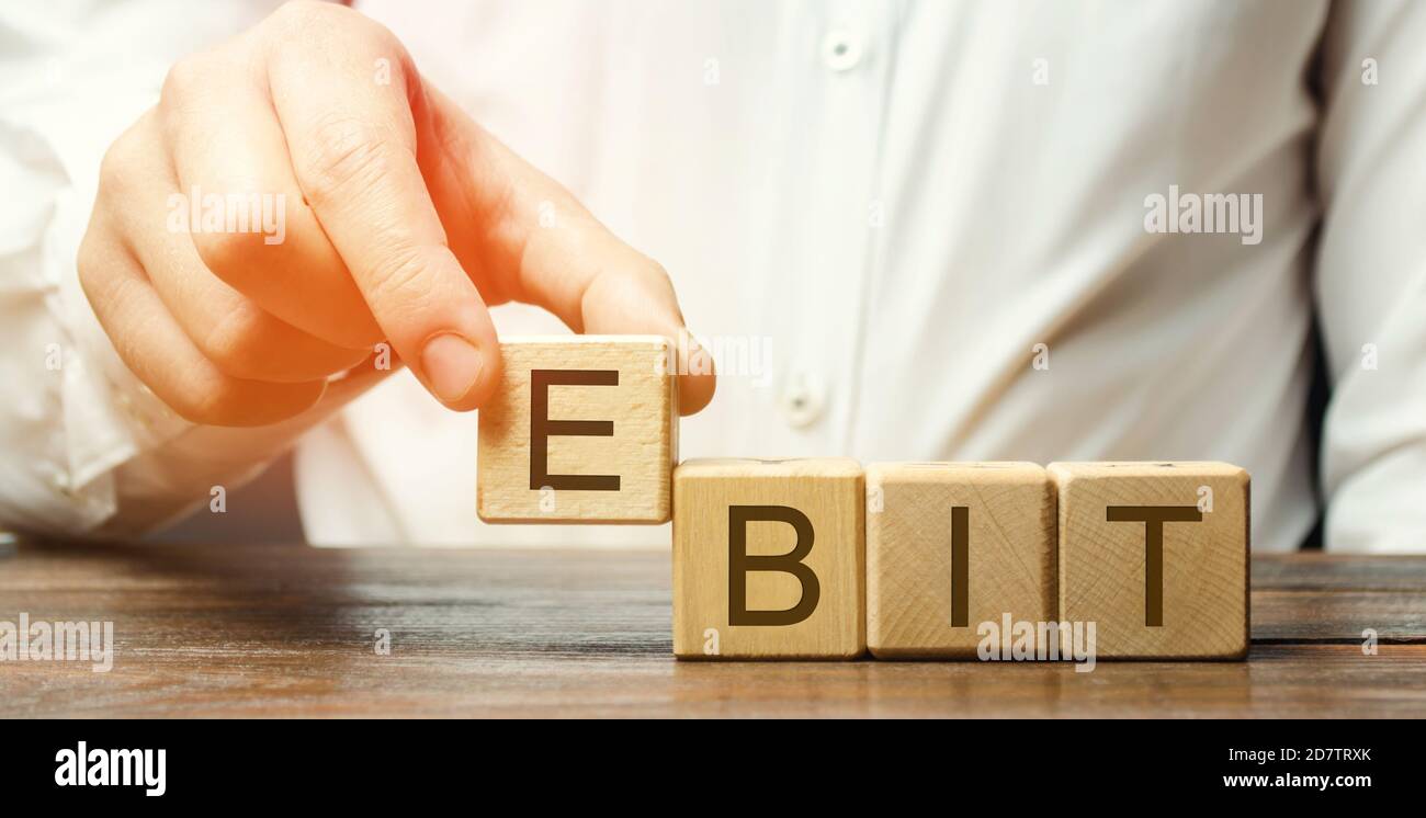 Businessman mette blocchi di legno con la parola EBIT - guadagni prima di interessi e tasse. Misura del profitto di un'azienda che include tutti i redditi e le spese. Foto Stock