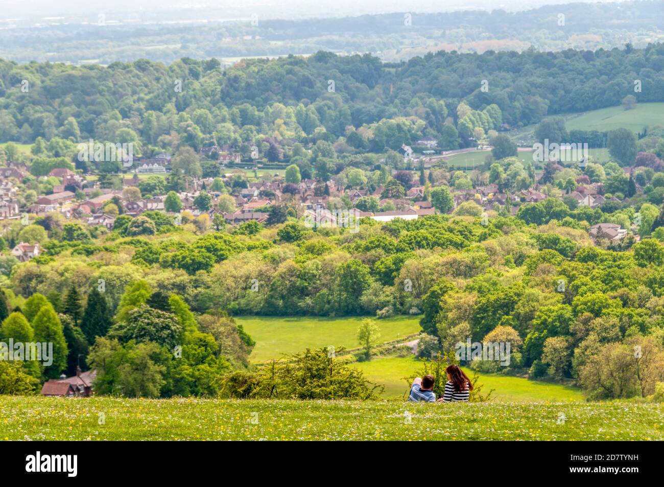 Persone che si siedono sull'erba guardando la vista della città suburbana di Reigate da Reigate Hill nella cintura verde di Londra. Foto Stock