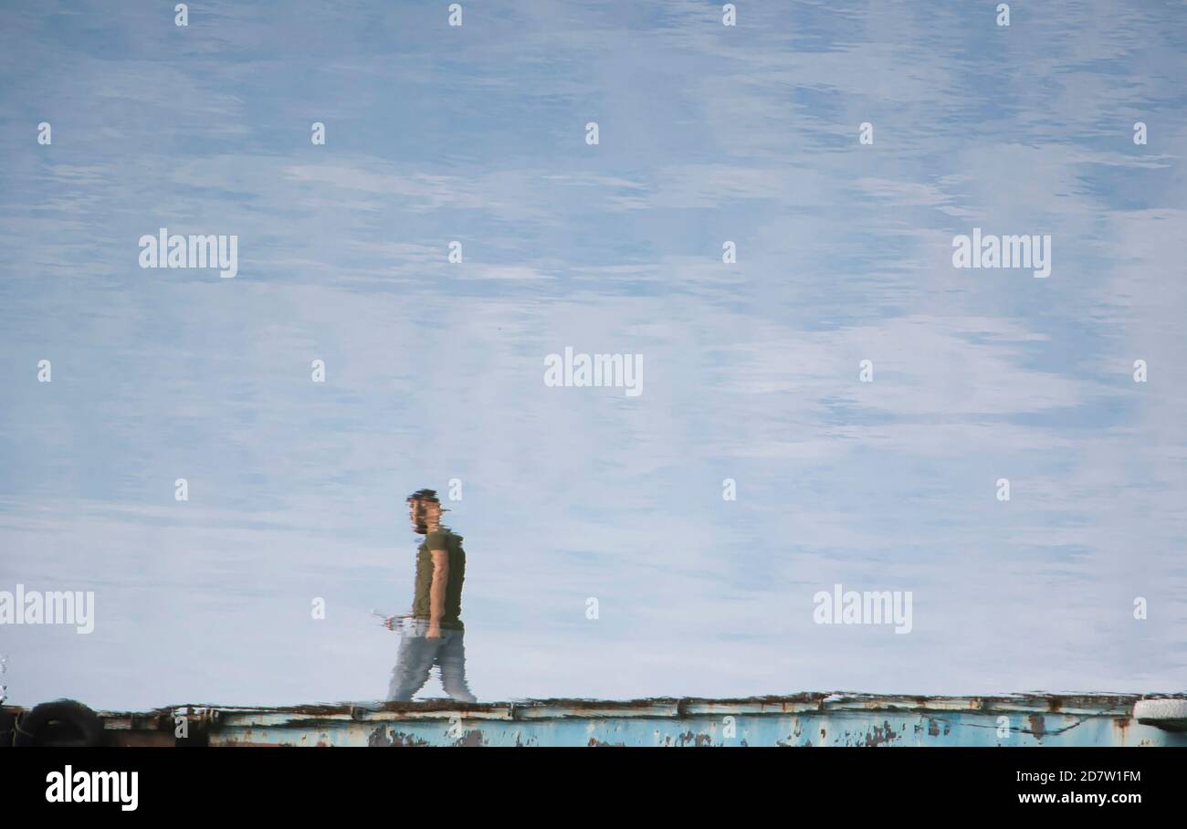 Riflessione in acqua di un giovane uomo che cammina su un molo del lago plotoon Foto Stock