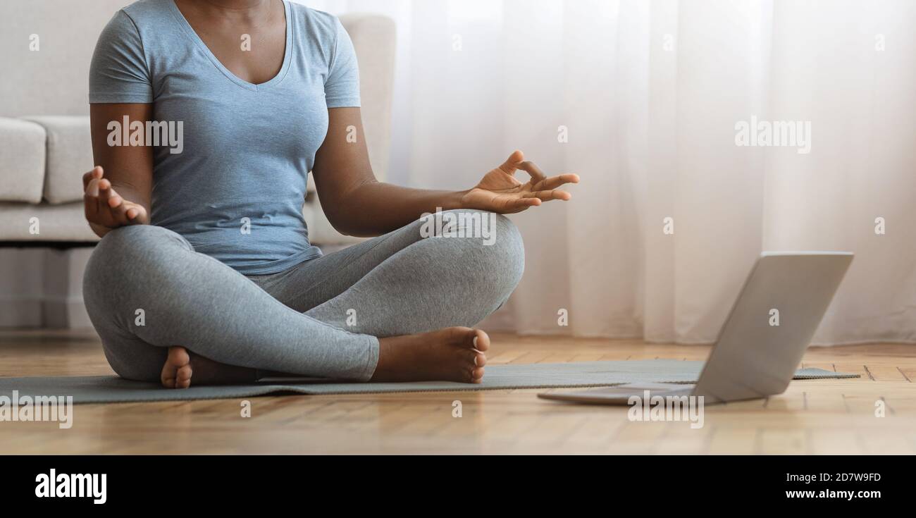 Meditazione online. Calma donna nera praticare lo yoga a casa con il suo laptop Foto Stock