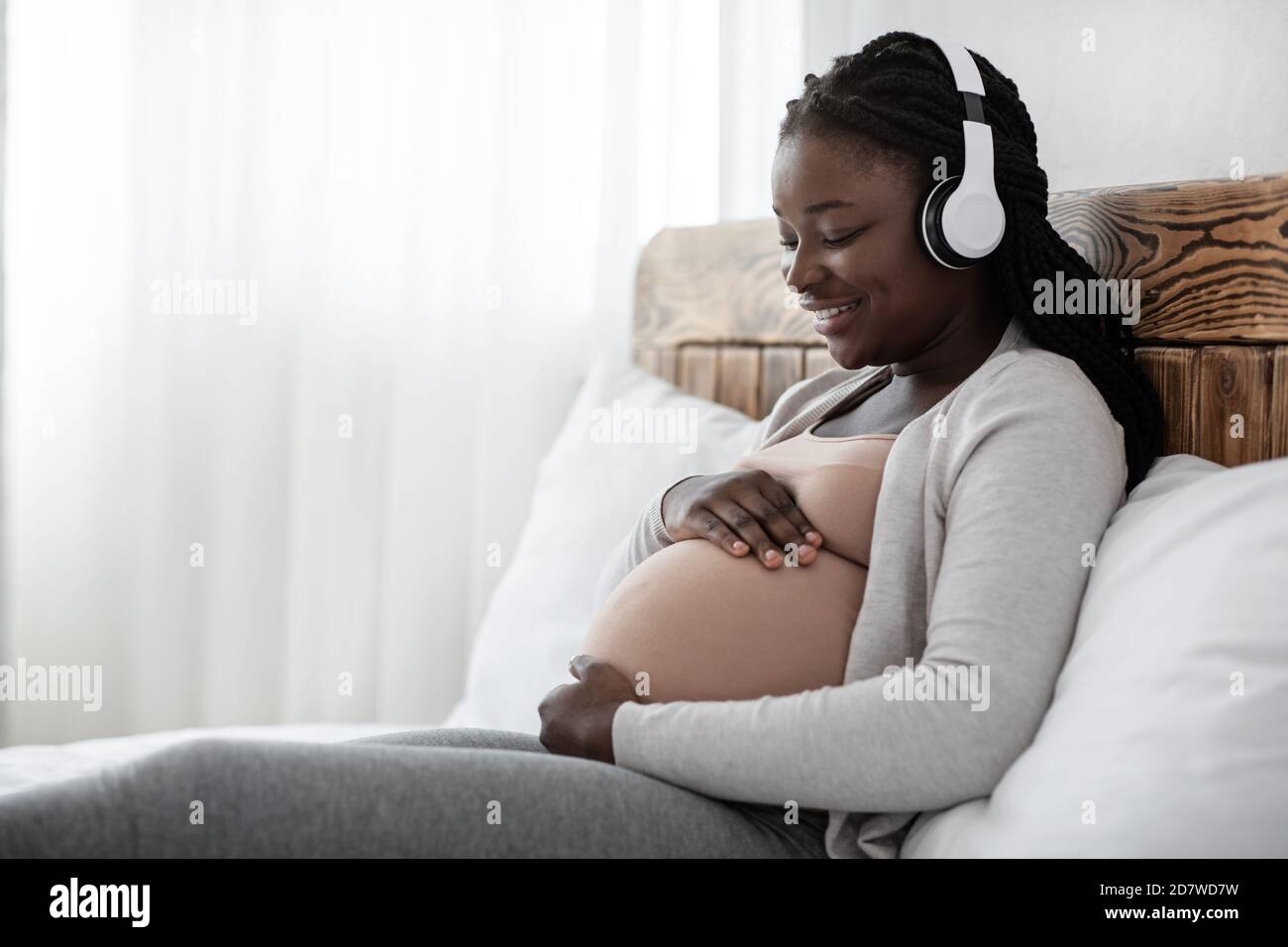 Passatempo di gravidanza. Donna incinta nera seduta sul letto ascolto di  musica nelle cuffie Foto stock - Alamy