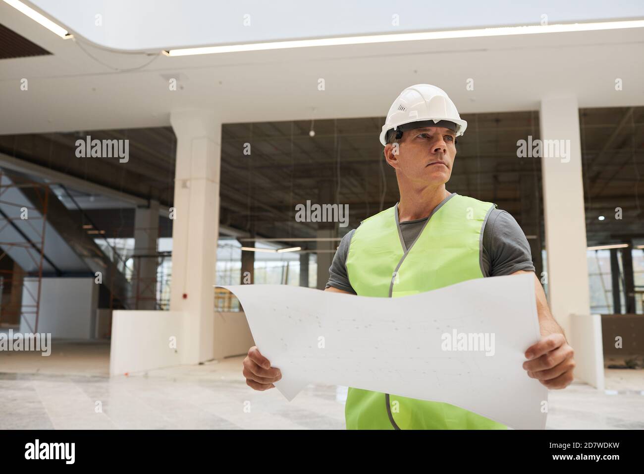 Ritratto in vita di operai edili professionisti che tengono piani e guardando lontano mentre si trova in ufficio edificio, copia spazio Foto Stock