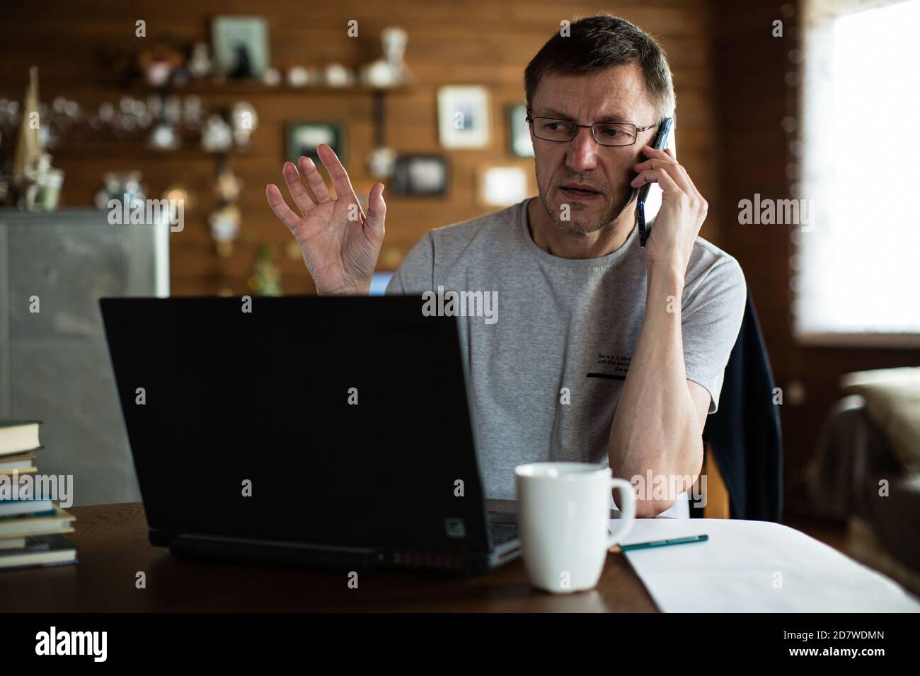 Uomo medio adulto seduto davanti al computer portatile e che parla al telefono. Foto Stock