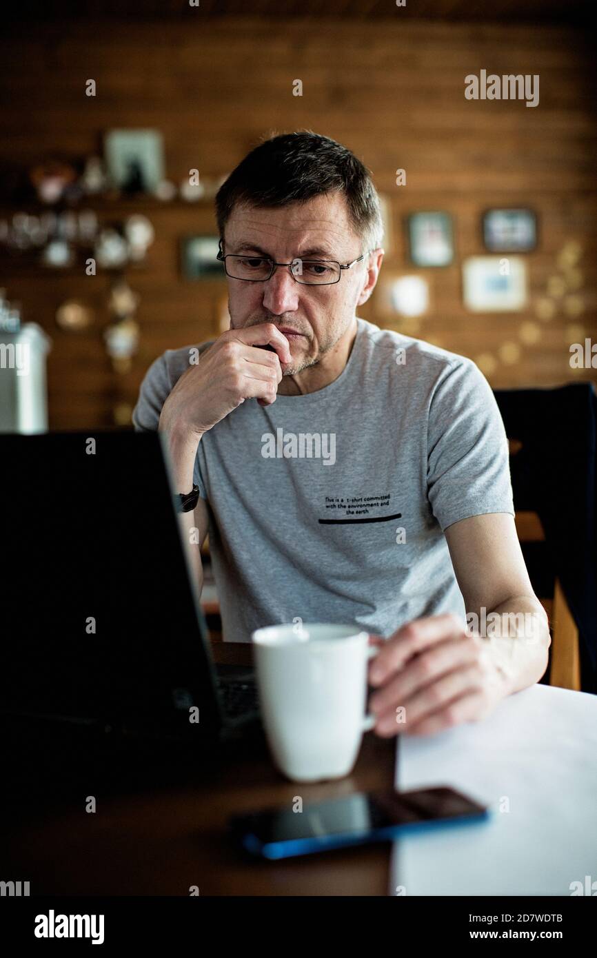 L'uomo mid adult si siede a un tavolo, guarda una tazza e pensa. Foto Stock