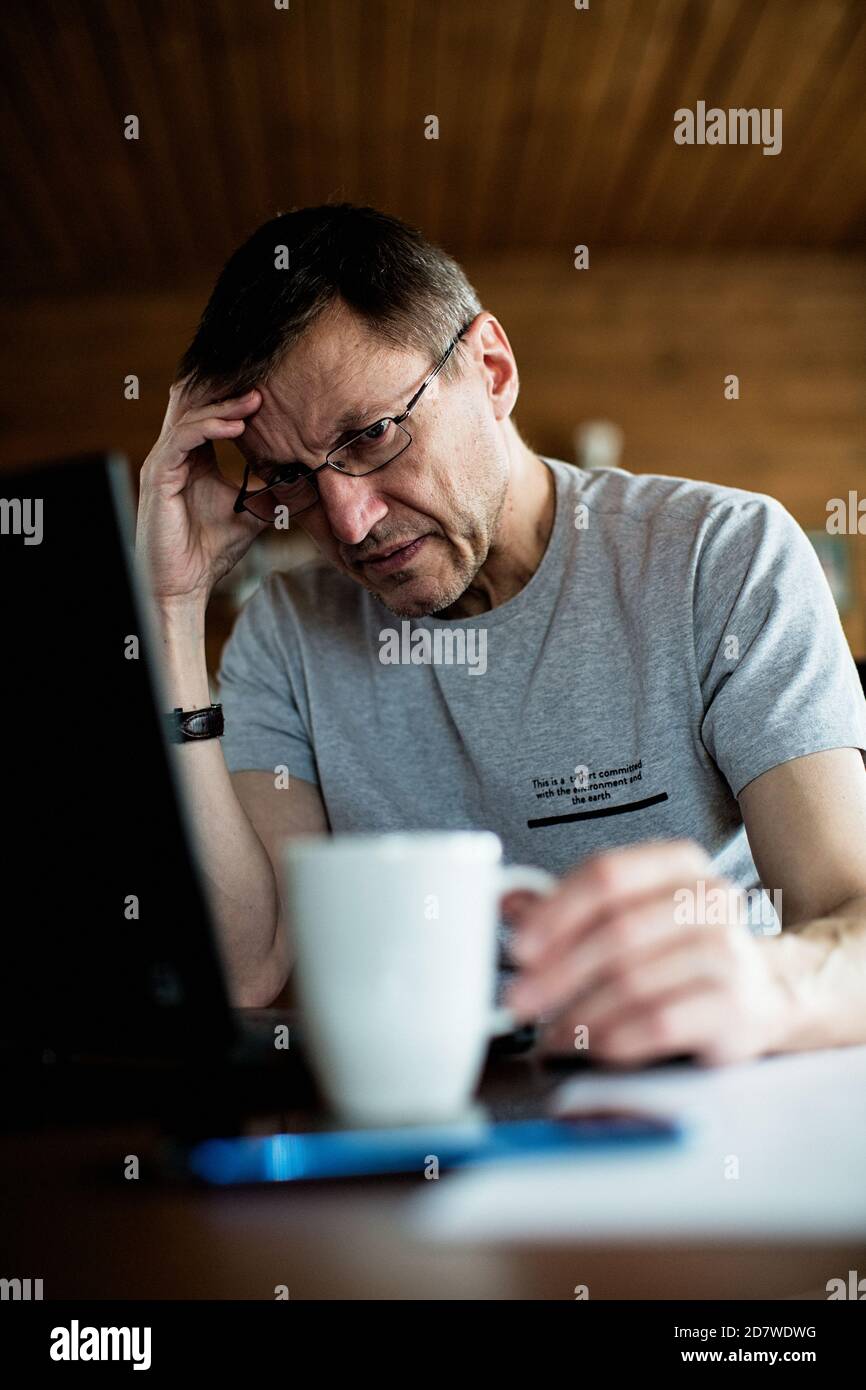 L'uomo mid adult si siede a un tavolo, guarda una tazza e pensa. Foto Stock