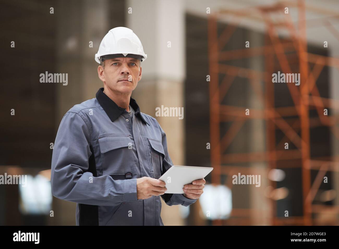 Ritratto in vita di un lavoratore maturo che tiene un tablet digitale e guarda la fotocamera mentre si trova in cantiere o in officina industriale, spazio di copia Foto Stock