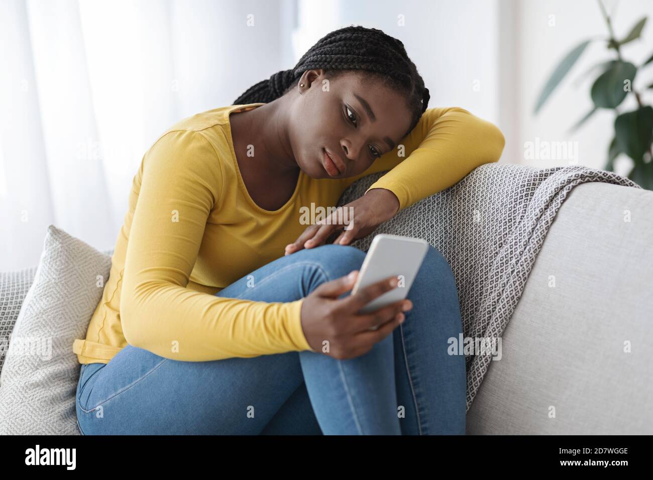 Sconvolto Donna africana seduta sul divano con smartphone, sentendosi Lonely e depresso Foto Stock