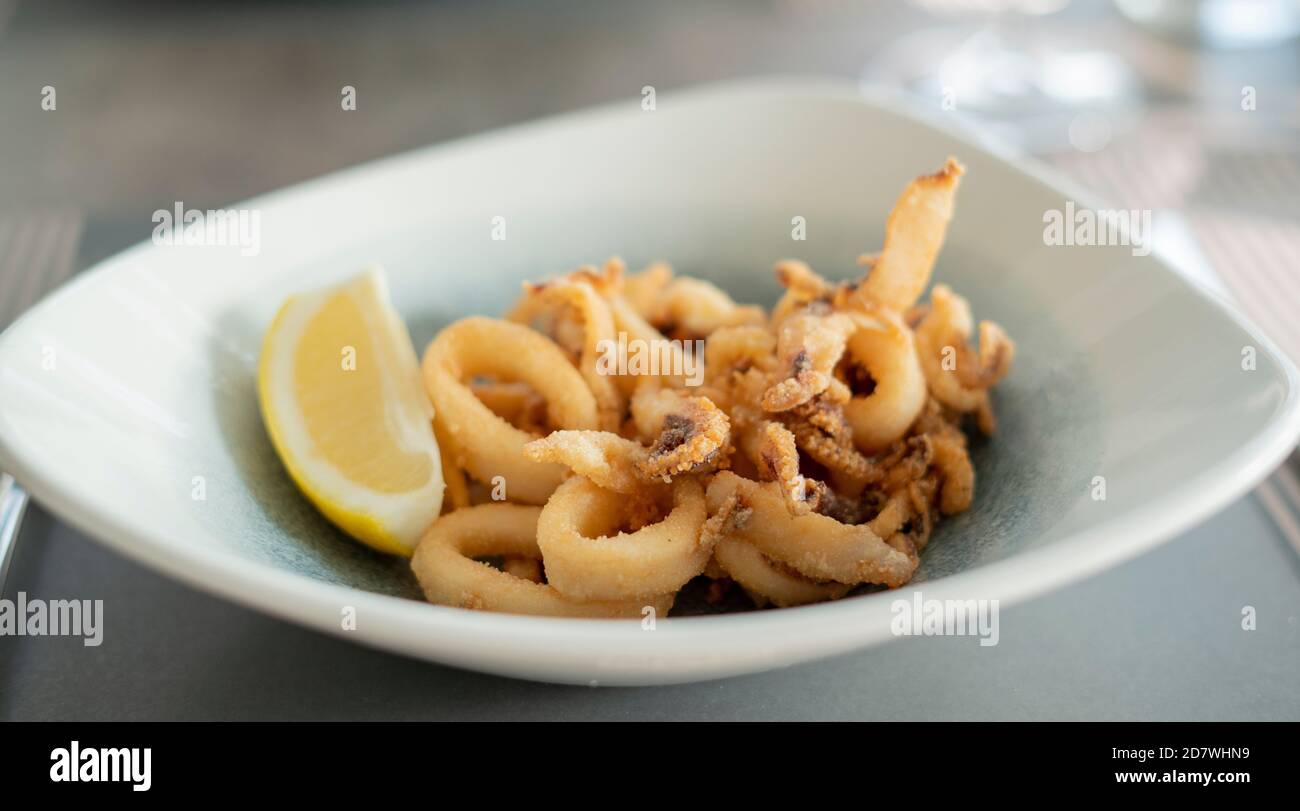 Primo piano di deliziosi calamari croccanti e fritti con limone su un piatto bianco. Foto Stock