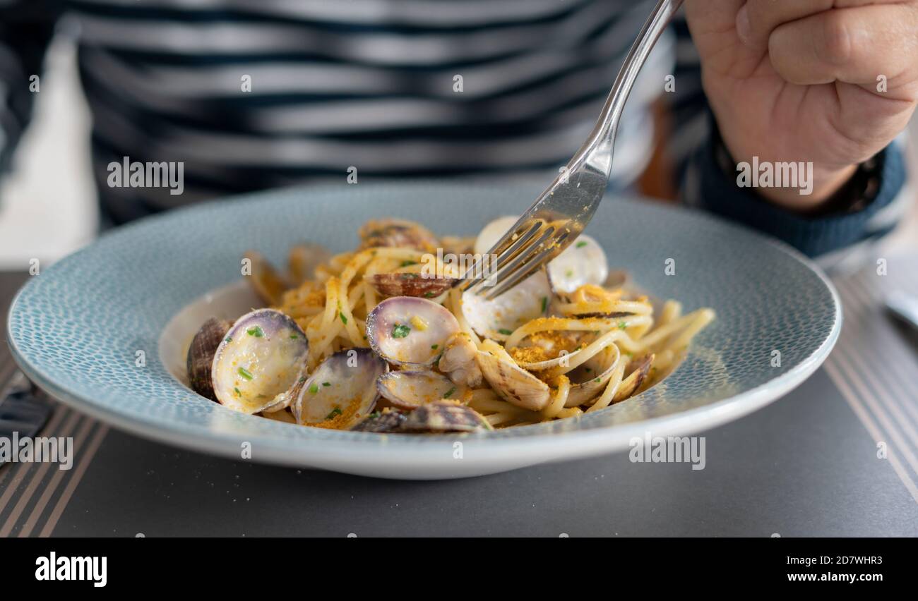 Dettaglio mano maschile mangiare spaghetti di pasta con vongole e triglie, cucina mediterranea Foto Stock