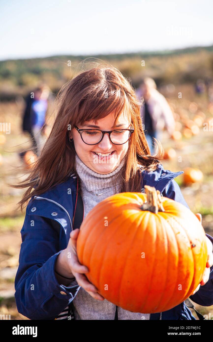 Una giovane donna che tiene e guarda una zucca che è appena selezionata, guardando felice con la sua scelta, pronta per Halloween. Foto Stock