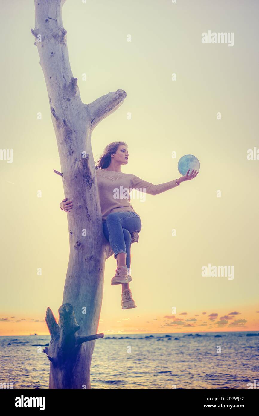 La ragazza tiene in mano la luna, il tramonto sul mare. I sogni diventano realtà. Foto Stock