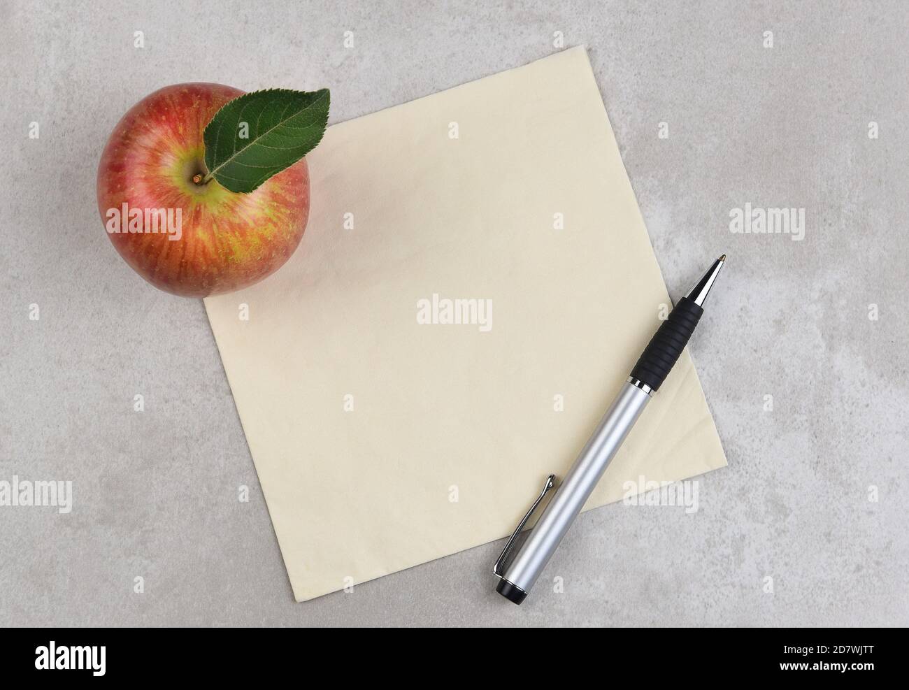Una mela, una penna e un tovagliolo su una superficie grigia con macchie. Spazio per la copia o il doodle sul tovagliolo. Foto Stock